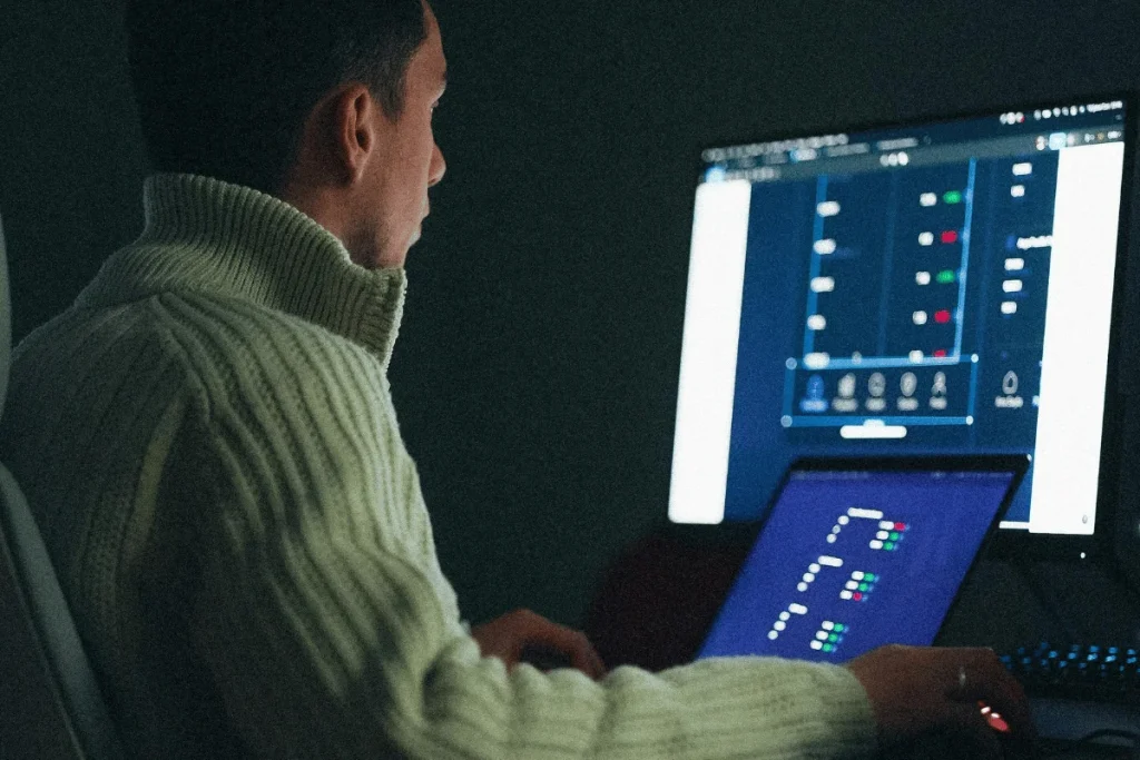 A person in a white sweater works intently on a computer in a dimly lit room.