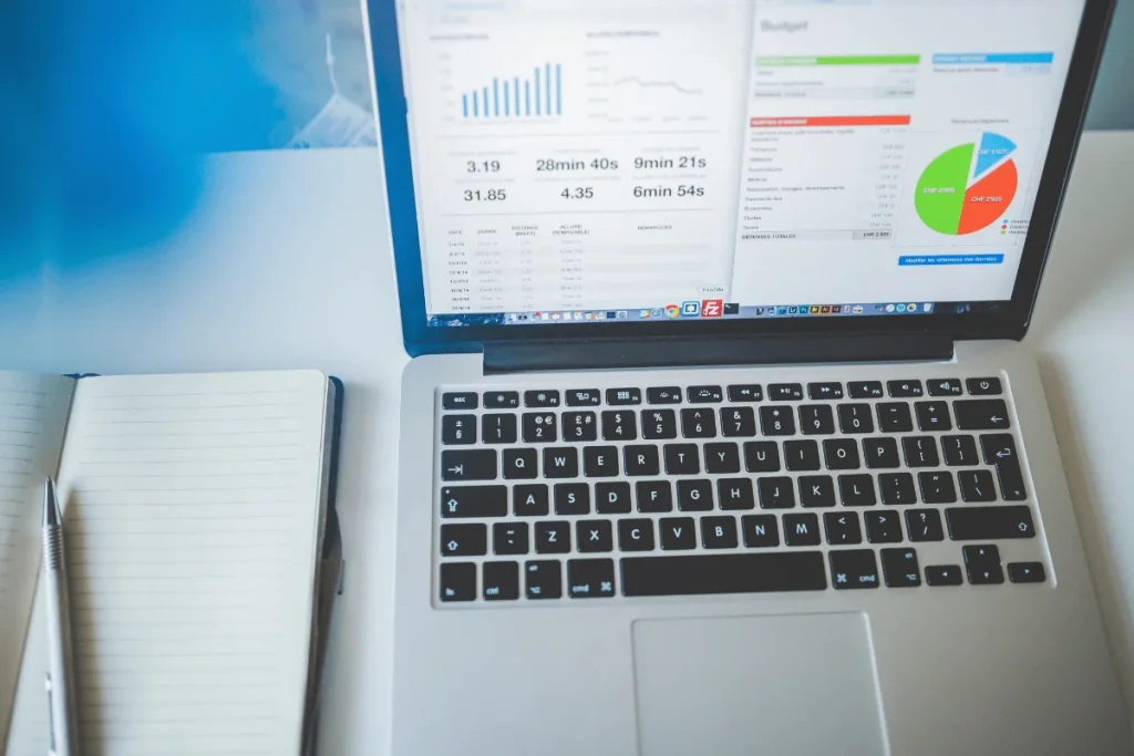 Budget charts and performance reports shown on a laptop beside a blank notebook.