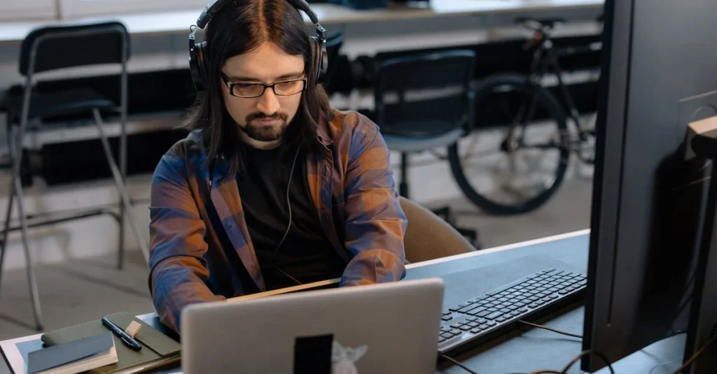 Developer with headphones using laptop for enterprise analytics platform development in modern office setting.