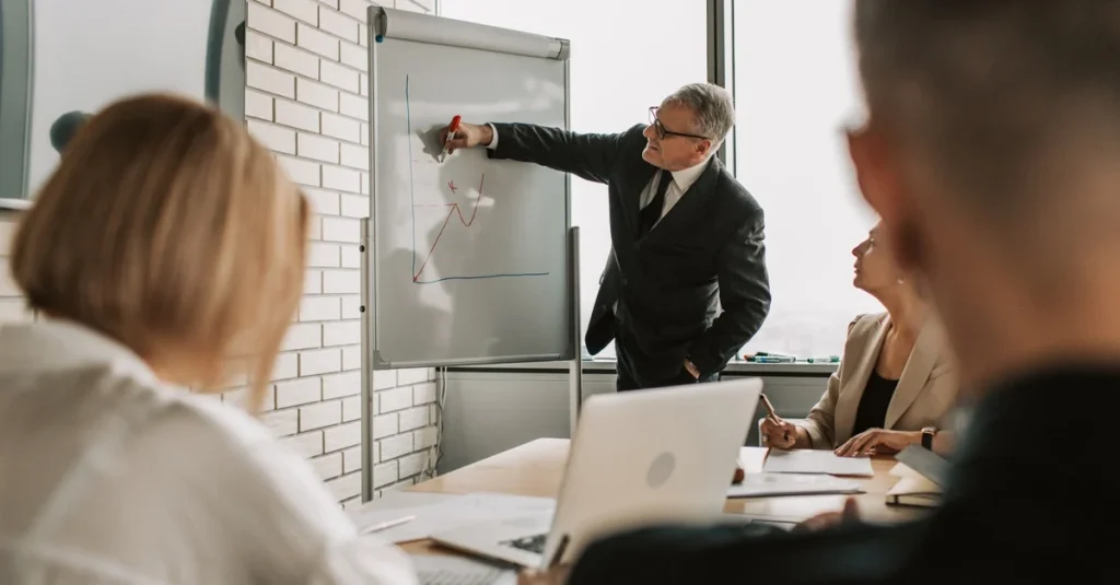 Business professional presenting data analytics ROI insights on whiteboard to engaged team during meeting.