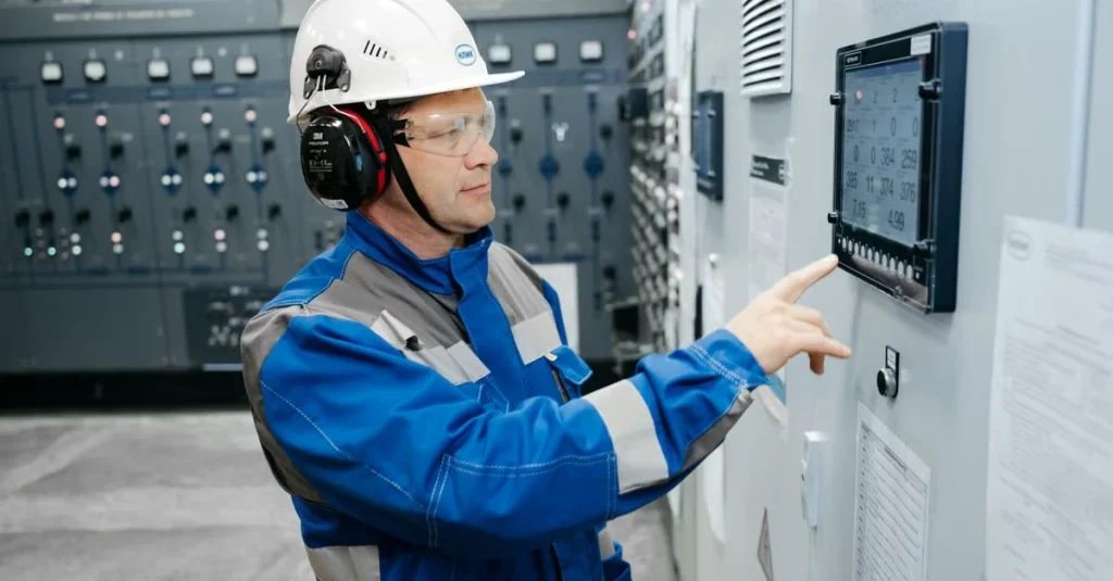 Technician in safety helmet monitoring advanced analytics manufacturing data on control panel display.