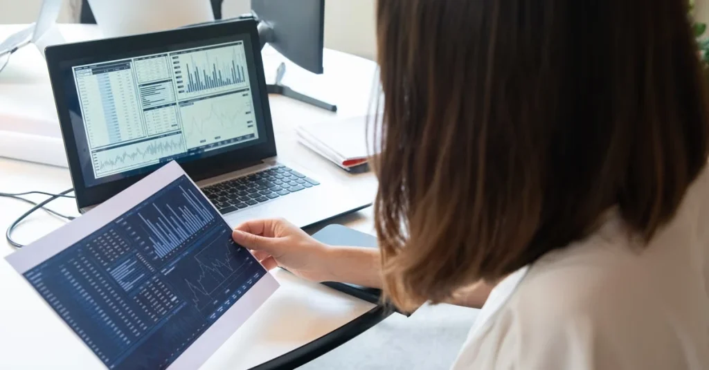 Woman analyzing advanced analytics manufacturing data on tablet and monitor at desk.