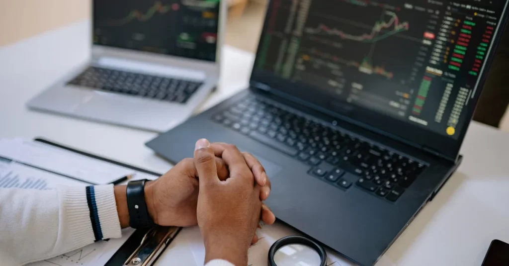 Trader hands together at desk with enterprise AI analytics platform charts displayed on dual monitors.